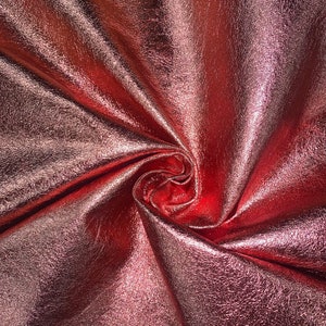 May include: Close-up of a metallic rose gold fabric with a textured surface. The fabric is folded and draped, creating a soft, flowing look.