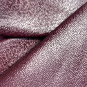 May include: Close-up of a deep burgundy leather fabric with a textured, pebbled surface. The fabric is folded in half, showing the texture from both sides.