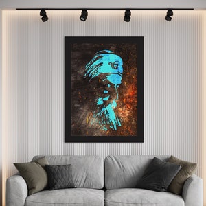 Op de afbeelding: Een ingelijste wandkunstprint met een gestileerd portret van een man met een lange baard en tulband. Het kunstwerk gebruikt een turquoise en oranje kleurenpalet tegen een donkere achtergrond. De print wordt boven een grijze bank weergegeven.