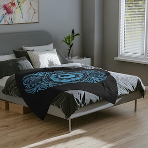 May include: A black and blue throw blanket with a circular mandala design. The blanket is on a bed with gray bedding.