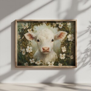 Könnte beinhalten: Gerahmter Kunstdruck mit einem weißen Kalb mit rosa Ohren, umgeben von einem Kranz aus weißen Blüten und grünen Blättern. Das Kunstwerk hat einen weichen, malerischen Stil mit einer hellen Farbpalette.