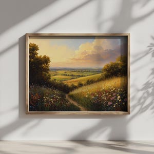 May include: A framed landscape painting depicts a sunlit valley with rolling hills and a winding path. The artwork features a vibrant color palette of greens, yellows, and blues, with a warm, golden light illuminating the scene. The frame is made of light-colored wood.