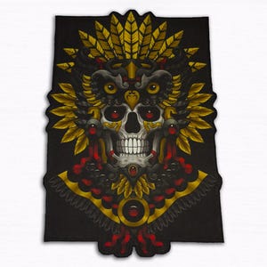 Op de afbeelding: Zwart rechthoekig embleem met een gedetailleerd schedelontwerp. De schedel heeft rode ogen en is versierd met een gevederde hoofdtooi in goud en zwart. Het ontwerp bevat ingewikkelde details en een decoratieve kraag.