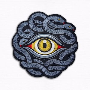 May include: Embroidered patch featuring a central eye design with a yellow iris and red accents, encircled by intertwined gray snakes with red tongues. The patch has a black background and a detailed, textured appearance.