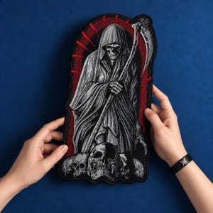 May include: A large embroidered patch featuring a hooded grim reaper figure holding a scythe, standing over a pile of skulls. The design uses black and white thread on a red background, enclosed within a dark arched border with a black edge.