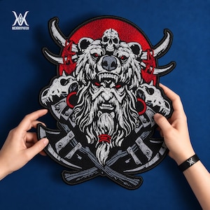 Könnte beinhalten: Ein bestickter Aufnäher mit einem bärtigen Krieger, der eine Bärenkopfbedeckung mit einem Totenkopf trägt, flankiert von zwei Tierschädeln und gekreuzten Äxten. Das Design umfasst einen großen roten kreisförmigen Hintergrund und detaillierte Stickereien.