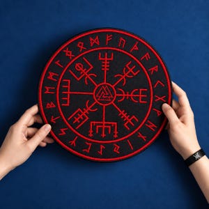 May include: A circular black embroidered patch featuring a red Vegvisir symbol at the center, surrounded by a ring of red runic characters. The design includes a central Valknut emblem, with intricate red line work forming the compass motif.