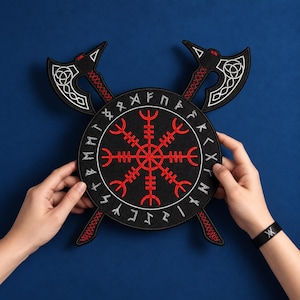 Könnte beinhalten: Ein kreisförmiger, schwarzer Stickaufnäher mit einem roten Vegvisir-Symbol in der Mitte, umgeben von einem Ring aus weißen Runenzeichen. Zwei gekreuzte schwarze Äxte mit weißen keltischen Knotenmustern und roten Akzenten liegen hinter dem Kreis.