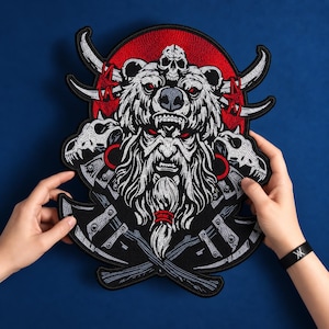 Könnte beinhalten: Ein großer gestickter Aufnäher mit einer bärtigen Figur, die eine Bärenkopfbedeckung mit einem Totenkopf trägt. Das Design zeigt zwei gekreuzte Äxte, zwei Tierschädel und einen leuchtend roten kreisförmigen Hintergrund in Schwarz und Weiß.