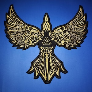 Könnte beinhalten: Ein gold gestickter Aufnäher mit einem stilisierten Vogel mit ausgebreiteten Flügeln. Der Vogel hat ein keltisches Knotendesign und ein Val-Knotensymbol auf seiner Brust. Der Aufnäher befindet sich auf einem blauen Hintergrund.