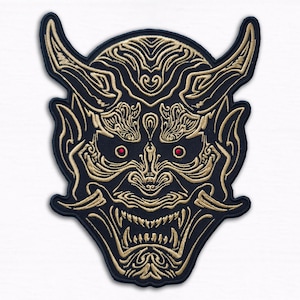 Può includere: Toppa ricamata raffigurante una maschera Oni. La maschera è prevalentemente nera con ricami color oro che delineano le corna, i denti e i motivi. Accenti rossi sono usati per gli occhi.