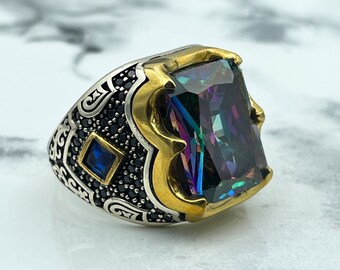 May include: A silver and gold ring with a large, faceted, iridescent gemstone. The ring is decorated with black stones and intricate designs.