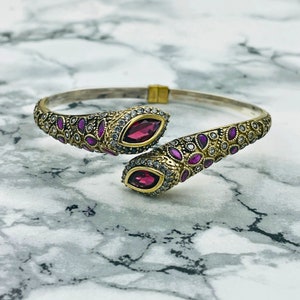 May include: A silver and gold bangle bracelet with a snake design. The bracelet is adorned with small pink and white gemstones.