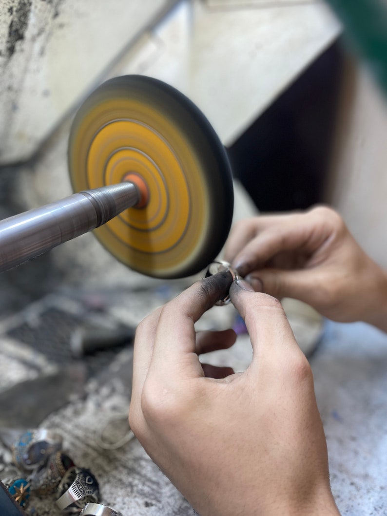 May include: A person's hand holding a silver ring against a spinning buffing wheel with a yellow and black surface.
