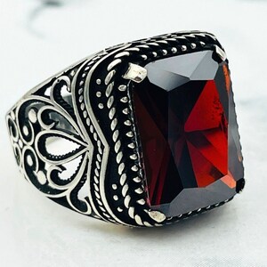 Könnte beinhalten: Ein silberner Ring mit einem verzierten Design und einem großen, roten Edelstein.