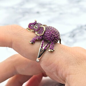 Peut inclure: Une bague en or avec un motif d'éléphant violet. L'éléphant est recouvert de petites pierres violettes.