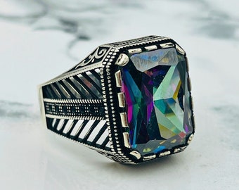 May include: A silver ring with an ornate design and a large, faceted, iridescent gemstone. The gemstone has shades of purple, blue, green, and gold.