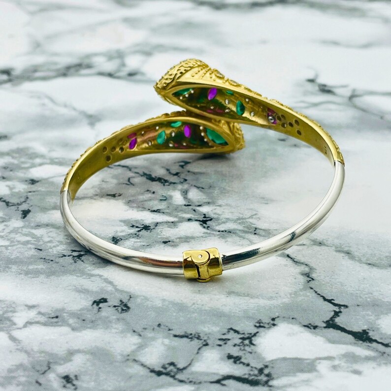 May include: A gold and silver snake bangle bracelet with green and pink gemstones. The bracelet is open and has a hinged clasp.