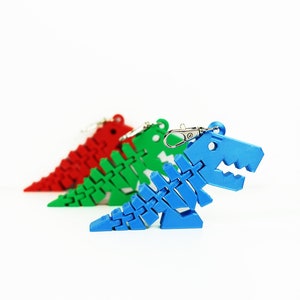 May include: Three plastic dinosaur skeleton keychains in red, green, and blue. The keychains are in a row, with the blue one in the foreground.