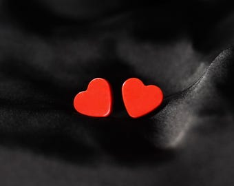 May include: Two red heart-shaped decorations on a black fabric background.