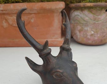 May include: A dark brown bronze sculpture of a deer head with antlers. The sculpture is detailed with intricate carvings and has a rustic finish.