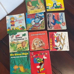 Könnte beinhalten: Eine Sammlung von acht alten Kinderbüchern mit bunten Umschlägen, die Illustrationen von Tieren, Zügen und Kindern zeigen. Die Bücher tragen die Titel "Vier Löwen beim Mittagessen", "Jürgens Ball", "Die Biene Maja", "Dieters Traumreise", "Kleiner Hund", "Jiminy Grille", "Was soll ich werden?" und "Peter kommt immer zu spät".