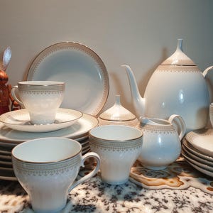 May include: A white porcelain tea set with gold trim. The set includes a teapot, creamer, sugar bowl, and six cups and saucers.