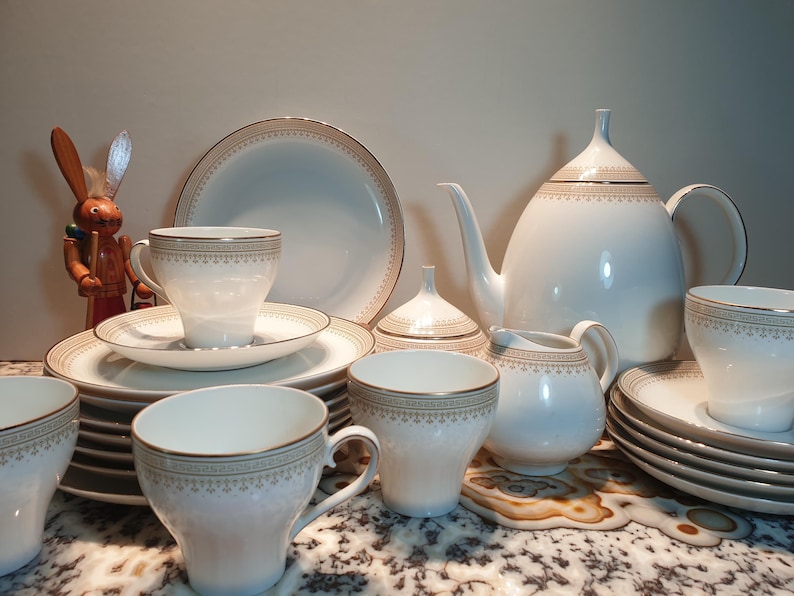 May include: A white porcelain tea set with gold trim. The set includes a teapot, creamer, sugar bowl, and six cups and saucers.