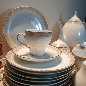 May include: A white tea set with gold trim. The set includes a teapot, creamer, sugar bowl, cups, and saucers. The teacups and saucers have a delicate floral pattern.