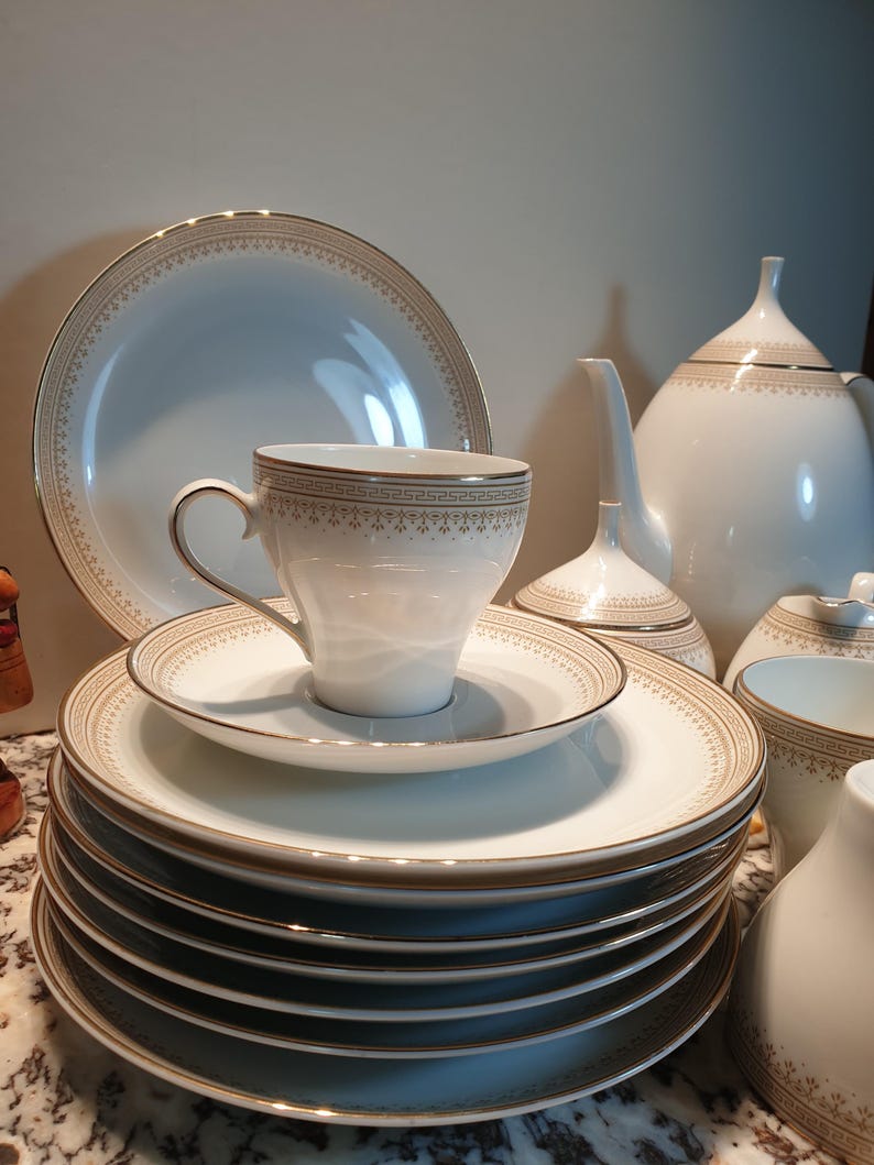 May include: A white tea set with gold trim. The set includes a teapot, creamer, sugar bowl, cups, and saucers. The teacups and saucers have a delicate floral pattern.
