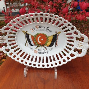 Può includere: Piatto da portata ovale in porcellana bianca con un design a traliccio. Il centro presenta un design decorativo con una stella rossa e il testo "In Treue fest. 1914-17 Weltkrieg."