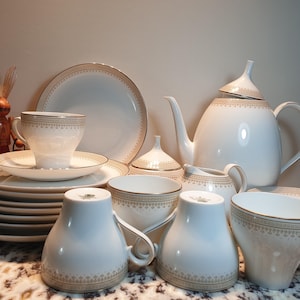 May include: A set of white porcelain teacups and saucers with gold trim and a matching teapot and sugar bowl. The teacups and saucers have a delicate floral pattern.