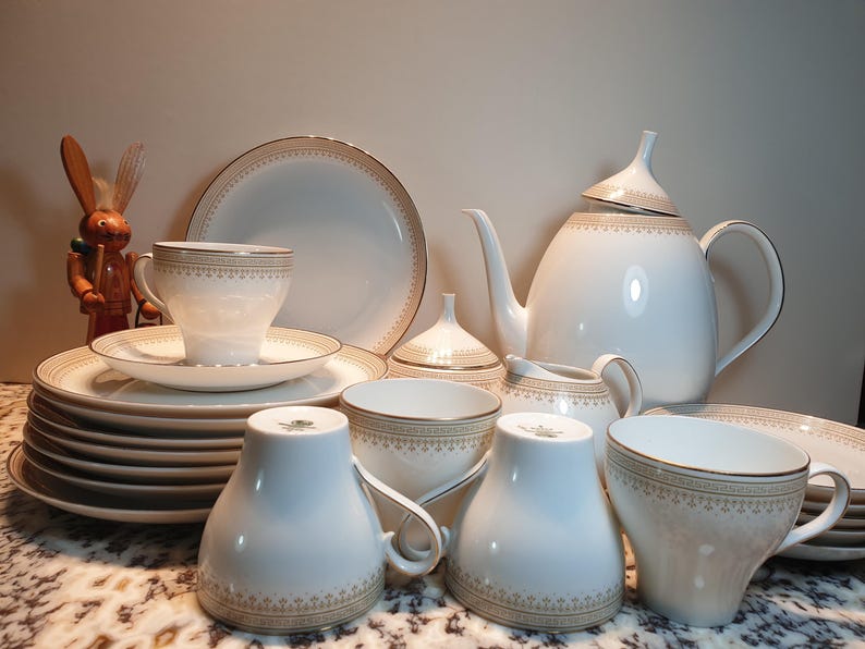 May include: A set of white porcelain teacups and saucers with gold trim and a matching teapot and sugar bowl. The teacups and saucers have a delicate floral pattern.