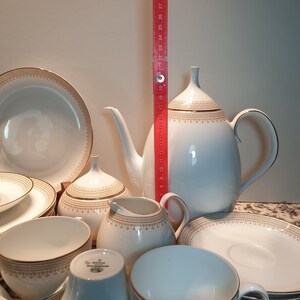 May include: A white porcelain tea set with gold trim. The set includes a teapot, creamer, sugar bowl, cups, and saucers. The set is decorated with a delicate floral pattern.