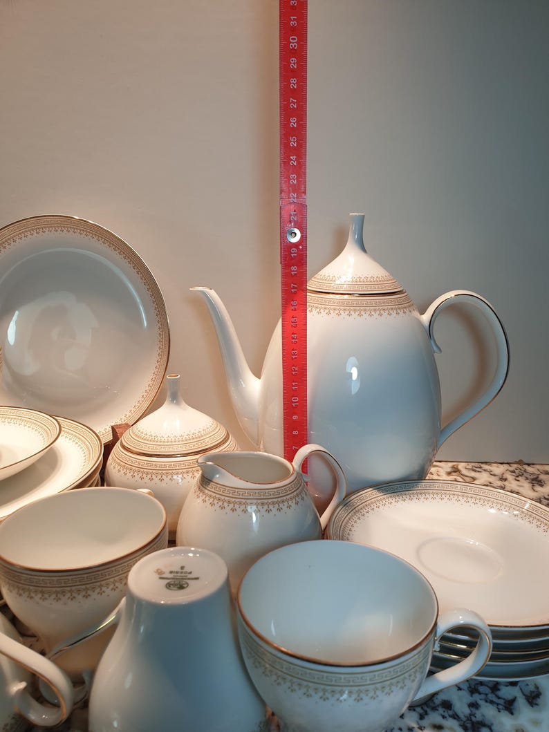 May include: A white porcelain tea set with gold trim. The set includes a teapot, creamer, sugar bowl, cups, and saucers. The set is decorated with a delicate floral pattern.