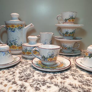 May include: A white tea set with floral designs in blue, yellow, and green. The set includes a teapot, creamer, sugar bowl, and four cups and saucers.