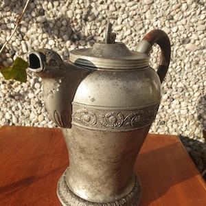 May include: A silver teapot with an ornate design and a bird-shaped spout. The teapot has a wooden handle and a lid with a finial.
