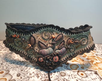 Könnte beinhalten: Ein dekorativer Gürtel mit aufwendigen Blumendesigns und bunten Perlen. Der Gürtel ist aus einem dunklen Stoff mit einem gehäkelten Rand.