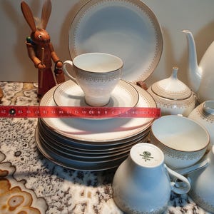 May include: A set of white porcelain teacups and saucers with gold trim and a delicate floral pattern. The set includes a teapot, creamer, and sugar bowl.
