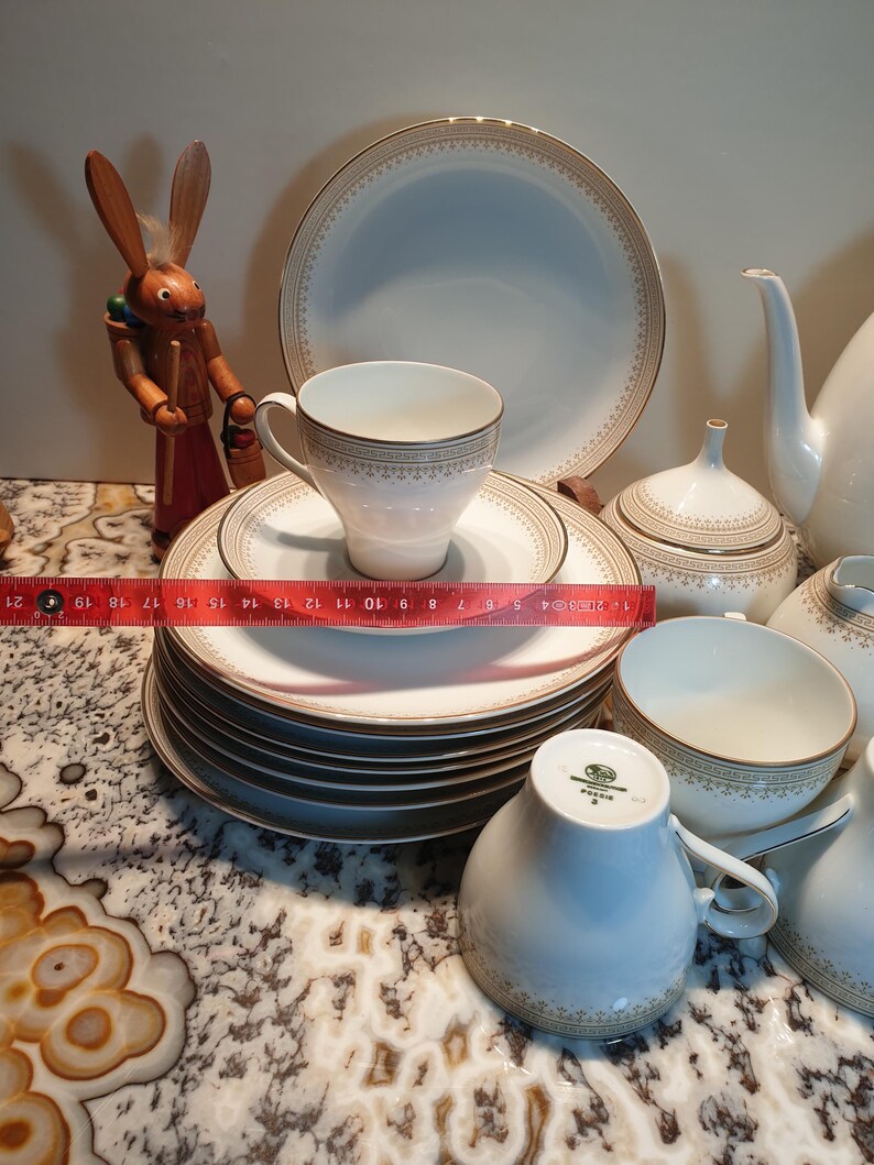 May include: A set of white porcelain teacups and saucers with gold trim and a delicate floral pattern. The set includes a teapot, creamer, and sugar bowl.