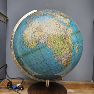 Peut inclure: Un globe terrestre sphérique présentant une carte détaillée de l'Afrique et des océans environnants, monté sur une base circulaire en bois foncé. Le globe comprend un méridien métallique gradué et un cordon électrique avec une prise.