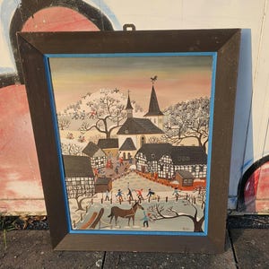 Può includere: Dipinto di arte popolare incorniciato raffigurante una scena di villaggio invernale. L'opera presenta una chiesa con un campanile, alberi innevati e figure impegnate in attività all'aperto. Il dipinto è ambientato in una cornice marrone scuro con un bordo interno blu.