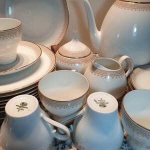 May include: A white porcelain tea set with gold trim. The set includes a teapot, creamer, sugar bowl, cups, saucers, and a plate. The set is decorated with a delicate floral pattern.