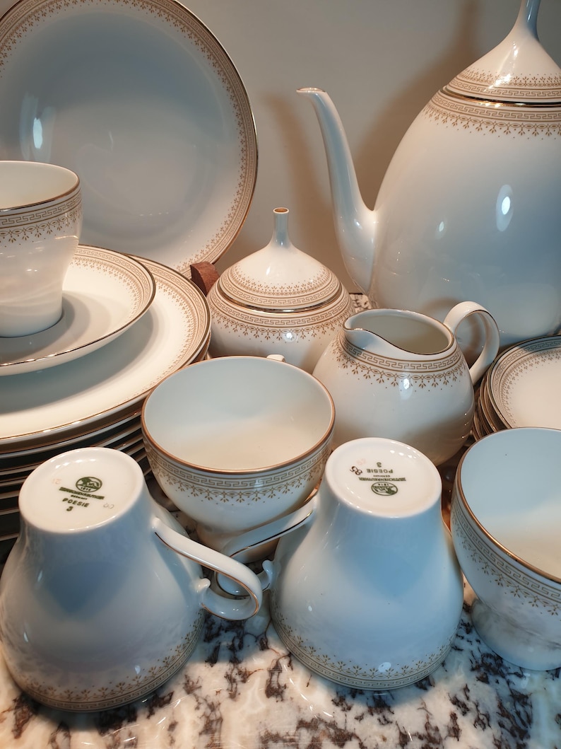 May include: A white porcelain tea set with gold trim. The set includes a teapot, creamer, sugar bowl, cups, saucers, and a plate. The set is decorated with a delicate floral pattern.