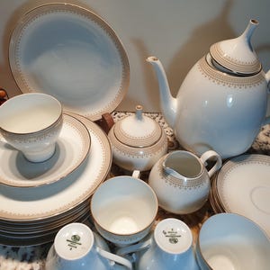 May include: A white porcelain tea set with gold trim. The set includes a teapot, creamer, sugar bowl, cups, and saucers.
