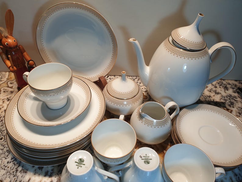 May include: A white porcelain tea set with gold trim. The set includes a teapot, creamer, sugar bowl, cups, and saucers.