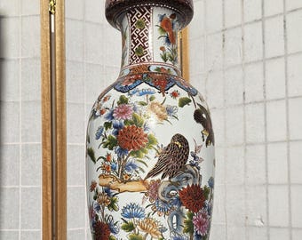 May include: A tall ceramic vase with a white base featuring intricate hand-painted details of brown birds perched on rocks, surrounded by vibrant red, blue, yellow, and green floral patterns. The neck and base have ornate geometric borders.