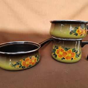 May include: A set of three vintage enamelware pots in shades of green and brown, adorned with hand-painted orange floral designs. The pots have black handles and silver rims, perfect for cooking.
