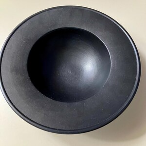 May include: A black ceramic bowl with a wide rim and a deep, rounded interior. The bowl is smooth and has a matte finish.