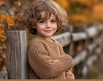 May include: A young child with curly blonde hair wearing a brown sweater stands next to a rustic wooden fence. The background is blurred and features autumn leaves in shades of yellow and orange.